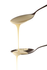 Condensed milk pouring from spoons, isolated on white