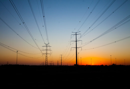 Silhouettes of power transmission line poles at sunset