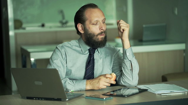 Young businessman eating apple and drinking coffee in office 
