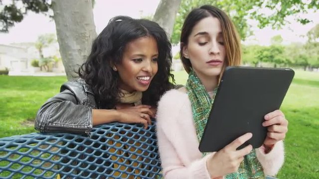 Best friends using tablet outdoors at a park