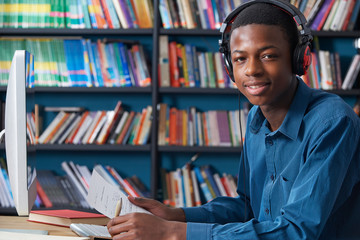 Male Teenage Student Working At Computer Wearing Headphones - obrazy, fototapety, plakaty