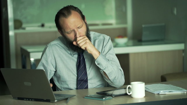 Sick businessman taking pill during work with laptop in office