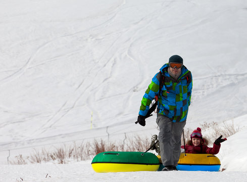 Father and daughter with snow tube at sun day