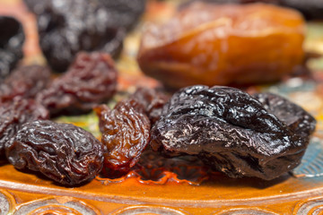 Different dried fruits as raisins and prunes, in front of a date, on a pottery tray with floral decoration