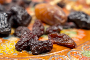 Several raisins in front of dates and prunes, on a pottery tray with floral decoration