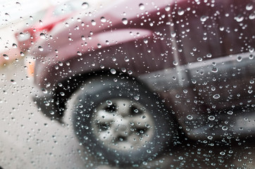 Wet car window with raindrops and a blurred car