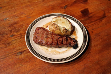 Strip Steak and Baked potato on old antique wooden table