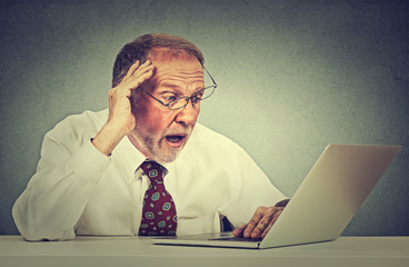 anxious senior man looking at laptop screen seeing bad news with disgusting emotion on his face