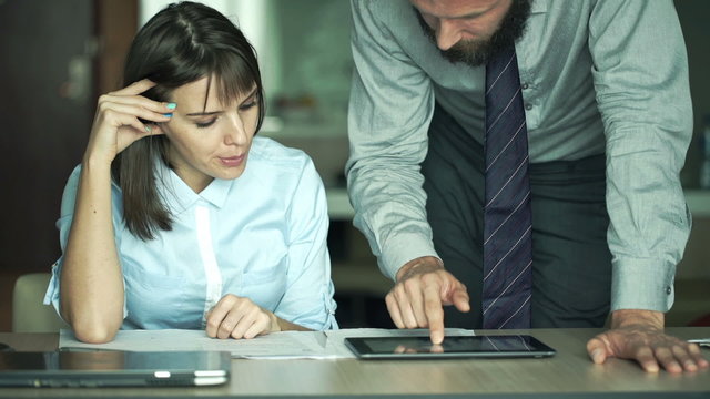 Businesspeople comparing data on tablet computer and documents in office
