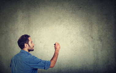 Business man young entrepreneur writing on a gray wall with pen