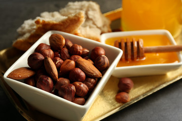 Glass jar and bowl with honey and nuts on gray background