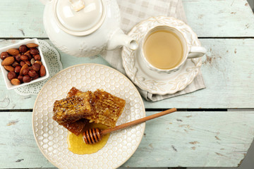 Honeycomb, bowl with honey, teapot and nuts on color wooden background