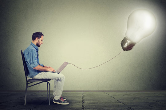 Young professional man using a laptop with light bulb plugged in it