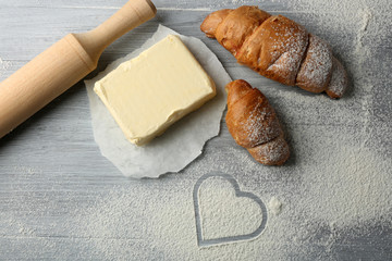Heart of flour, croissant and  wooden kitchen utensils on gray background