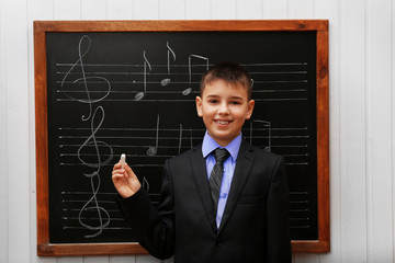 Young cute schoolboy standing at the blackboard with musical notes