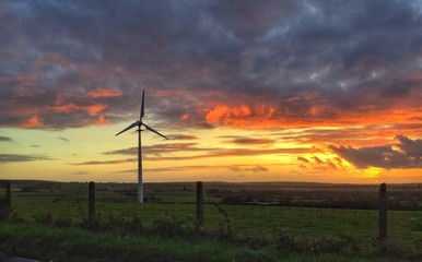 a single wind turbine against a setting sun