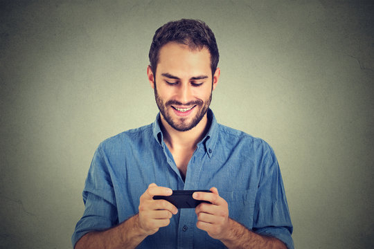 Smiling man looking at his smart phone while text messaging or watching video