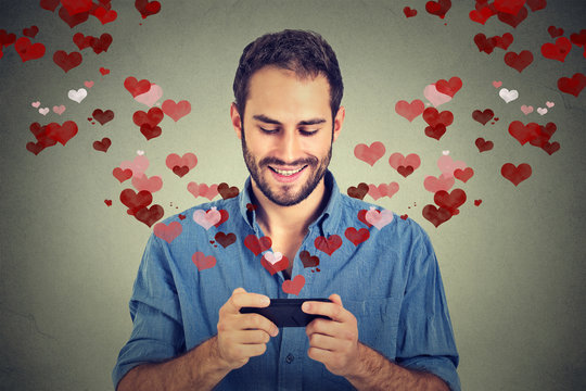 man sending love sms message on mobile phone with hearts flying away