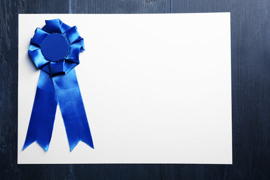 Award ribbon on white paper sheet, on wooden background