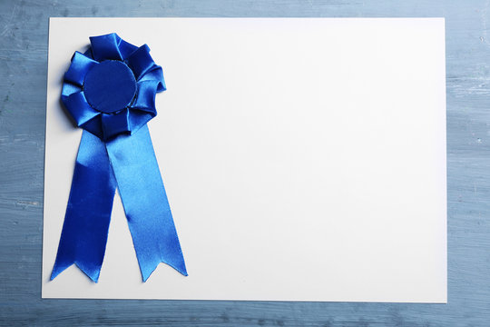 Award ribbon on white paper sheet, on wooden background