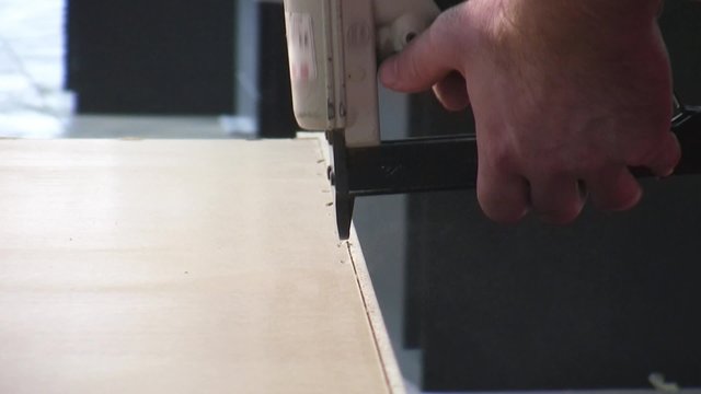 Worker using staple gun to fix back side of the closet in furniture factory.
