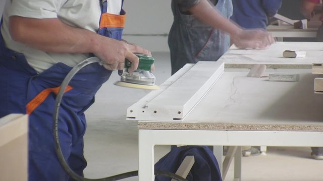 Worker using a power sander to smooth part of the doors frame.
