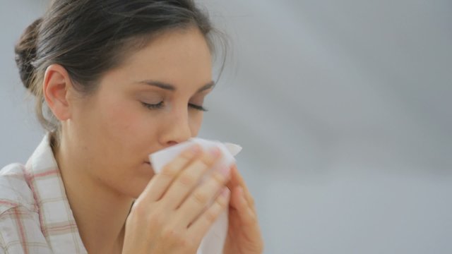 Young woman with cold blowing her nose