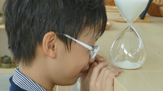 Little Asian boy looking at hourglass 
