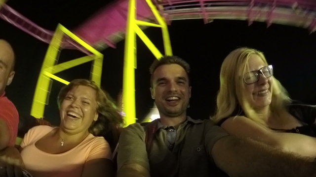 Happy people enjoying roller coaster ride in amusement park at night.