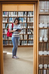 Pretty student with backpack reading a book in library