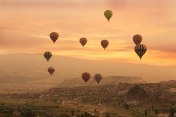 Multi-colored balloons fly over rocks in Cappadocia at sunrise