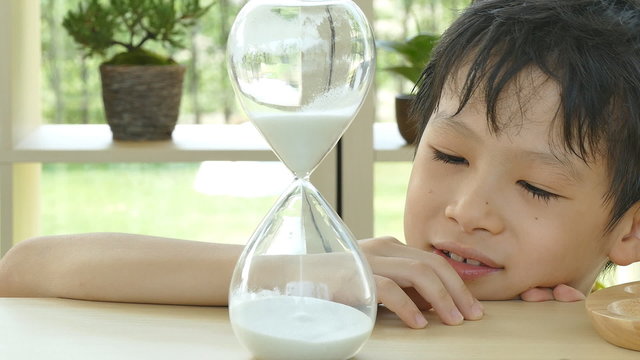 Little Asian boy looking at hourglass 

