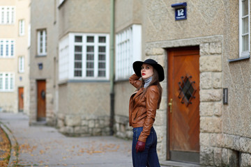 Fototapeta na wymiar Young woman with hat and leather jacket in front of an appartment building