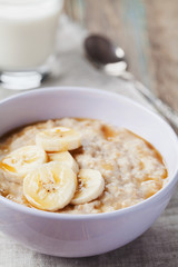 Bowl of oatmeal porridge with banana and caramel sauce on rustic table, hot and healthy breakfast every day, diet food