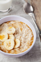 Naklejka na ściany i meble Bowl of oatmeal porridge with banana and caramel sauce on rustic table, hot and healthy breakfast every day, diet food