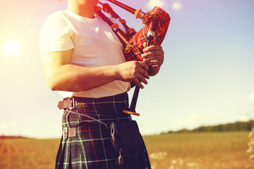 young man playing pipes in national uniform on green summer outdoors copy space background, closeup picture - obrazy, fototapety, plakaty