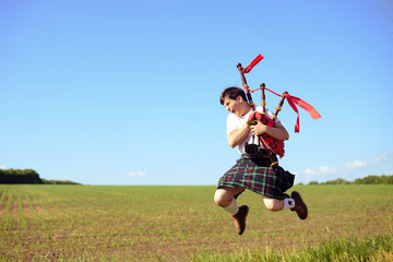 Picture of male jumping high with pipes in Scottish traditional kilt on green outdoors copy space...