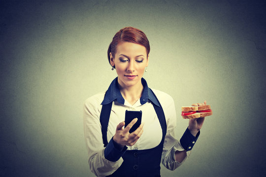 business woman reading news message on smart phone holding eating sandwich