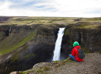 Woman in red jacket relax on cliff near fantastic waterfall