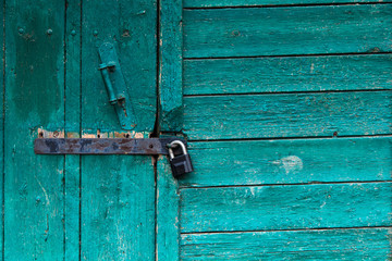 Old door locked up. Мetal lock. Bright turquoise peeling paint. Old wooden building.
