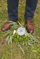 Young fashion man's legs in blue jeans and brown boots on grass with brides bouquet 