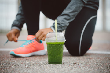 Detox smoothie drink and running footwear close up. City outdoor workout and fitness healthy nutrition concept.  Female athlete tying sport shoes laces before training. - 96245684