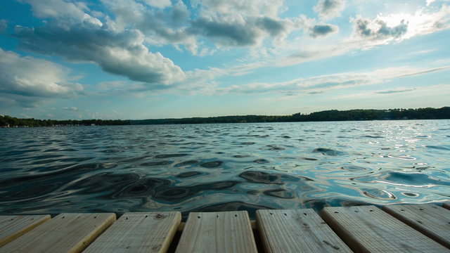 Lake End of Dock Dolly Sun Behind Clouds. camera moves left then right at the end of a dock overlooking the lake on a beautiful sunny summer day. Sun is hidden behind clouds.
