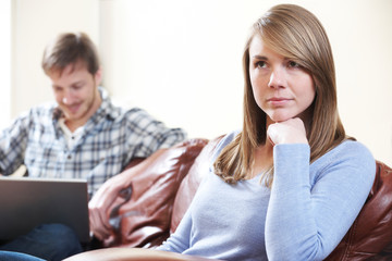 Unhappy Woman Sitting On Sofa As Partner Uses Laptop