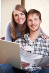 Happy Young Couple Looking At Finances On Laptop