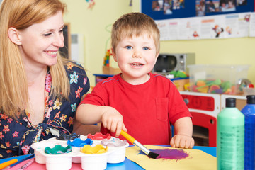 Teacher Helping Pre School Pupil In Art Class