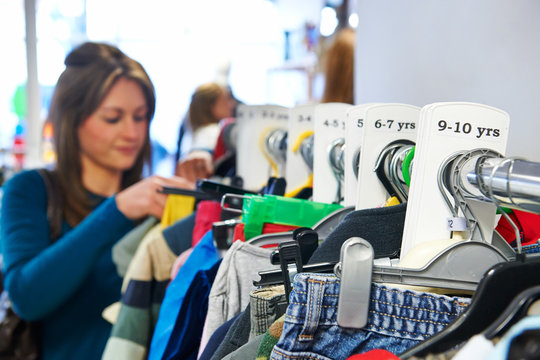 Woman Buying Children's Clothes In Charity Shop