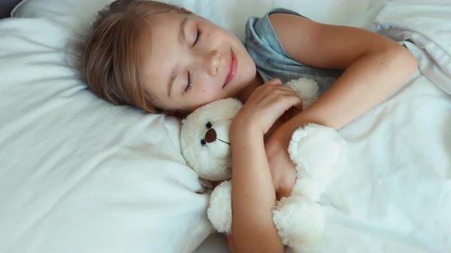 Portrait girl child sleeping with teddy bear in a bed and hugging toy. Top view