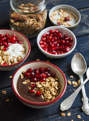 Healthy Breakfast - yogurt with homemade granola and pomegranate on a dark wooden board.