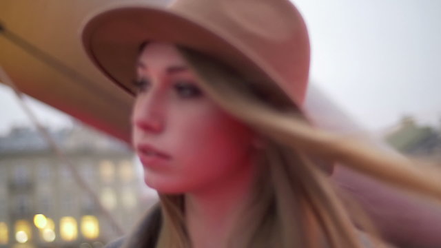 Beautiful white model walking in a city at dusk, hair moving on the wind, looking at camera and giving a gentle smile. Going in and out of focus, medium close-up.
